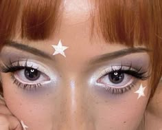 a woman with white stars painted on her face and eyelashes, holding up her hand to her cheek