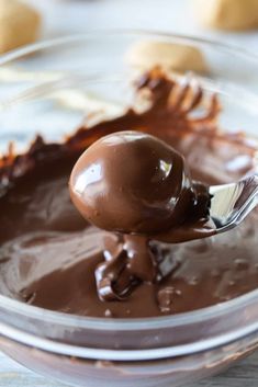 a spoon full of melted chocolate on top of a glass bowl with cookies in the background