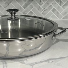 a stainless steel casserole sitting on top of a white marble counter with silver handles