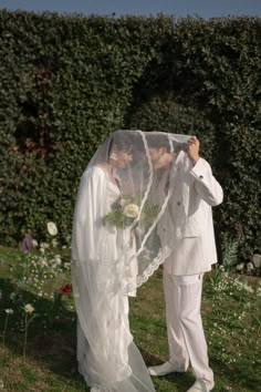 a bride and groom standing under a veil in front of a hedge covered with flowers