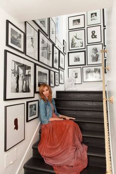 a woman sitting on top of a black and white stair case next to a bunch of framed pictures