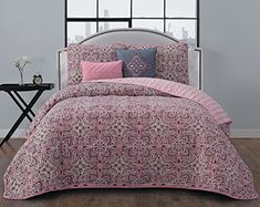 a bed with pink and blue comforters on top of it in front of a window