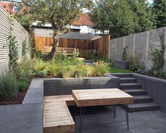 a table and benches in a backyard with trees, bushes and plants on the side