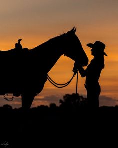 the silhouette of a man standing next to a horse in front of an orange sky