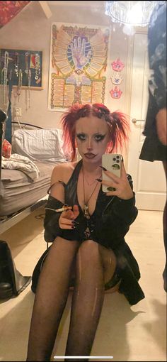 a woman with red hair and makeup sitting on the floor holding a cell phone in her hand