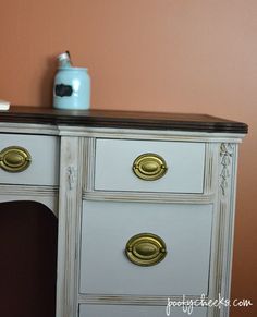 a white dresser with gold handles and knobs next to an orange wall in a room