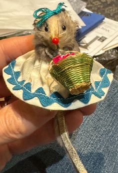 a small toy mouse sitting on top of a cloth covered plate with a basket in it's lap