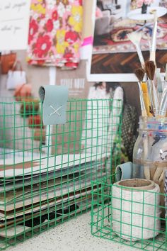 green wire baskets with pens and pencils in them on a counter next to other office supplies