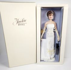 a barbie doll in a white dress and hat inside a box with the lid open