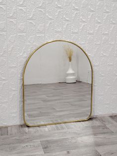 a white vase sitting on top of a wooden floor next to a gold framed mirror