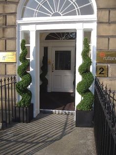 an entrance to a building with two topiary bushes on either side of the door