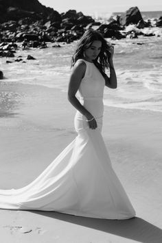 a woman standing on top of a beach next to the ocean wearing a white dress