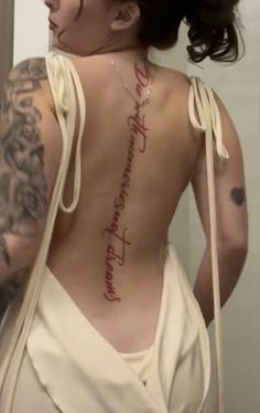 a woman with tattoos on her back is looking at herself in the mirror and has words written on her back