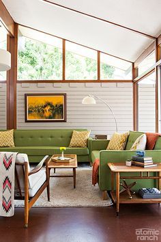 a living room filled with green couches and wooden tables on top of a hard wood floor