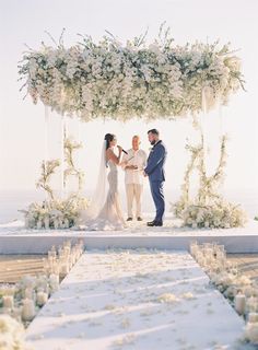 a man and woman standing under a white flower covered wedding arch