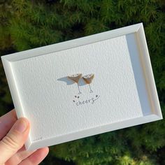 a person holding up a card with two birds on it's back and the words cheers written in front