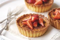 three small pies with strawberries on top are sitting on a plate next to a fork