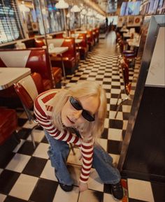 a woman with blonde hair and sunglasses leaning on a checkered floor in a restaurant