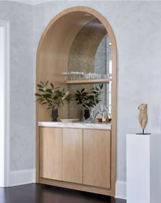 an arched wooden cabinet with plants and glasses on it in a room that has white walls