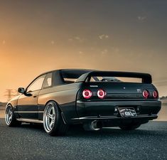 the rear end of a black sports car parked in front of a body of water