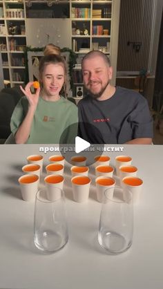 a man and woman sitting at a table with orange cups