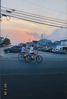 two people riding bikes down the street at sunset