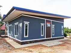 a small blue house sitting on top of a dirt field next to a building under construction