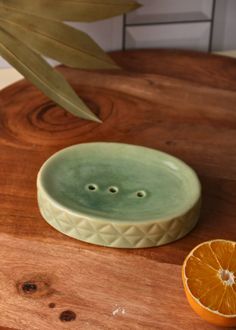 an orange sitting on top of a wooden table next to a green bowl with two holes in it