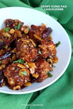 a white plate topped with meat covered in sauce and nuts on top of green cloth