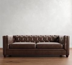 a brown leather couch sitting on top of a wooden floor next to a white wall