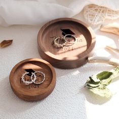 two wedding rings are placed in a wooden box on the floor next to some flowers