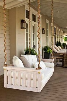 a porch swing with pillows on it and potted plants hanging from the front door