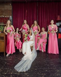 a bride and her bridal party posing for a photo in front of red curtains