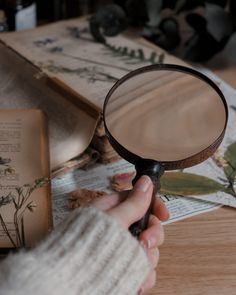 a person holding a magnifying glass over an open book on a wooden table