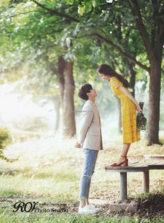 a woman in yellow dress standing next to a man on a bench