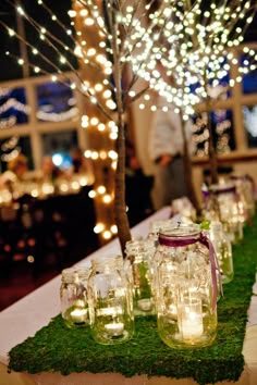 mason jars are lined up on a moss covered table runner with lights in the background