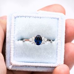 a person holding an engagement ring with a blue sapphire and three white diamonds on it