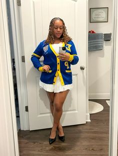 a woman standing in front of a white door looking at her cell phone while wearing a blue and yellow cardigan