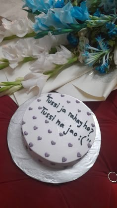 a cake with writing on it sitting next to flowers