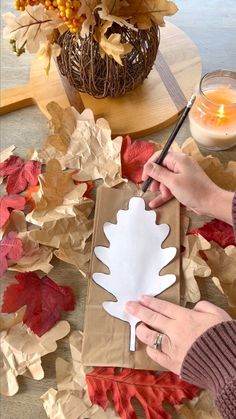 a woman is making a paper leaf craft with leaves around her and a candle in the background