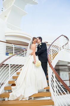 a bride and groom standing on the stairs of a cruise ship, posing for a photo