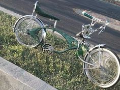 a green bicycle parked on the side of a road next to grass and street signs