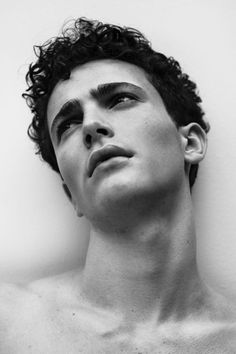 a man with curly hair and no shirt on is looking up at the sky in front of a white wall