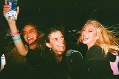 three girls are smiling and holding up their cell phones in the air while standing next to each other