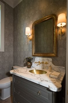 a bathroom with marble counter top and gold mirror above the sink, along with a toilet