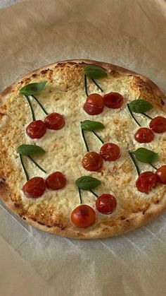 a pizza with cherry tomatoes and basil on it sitting on wax paper next to a knife