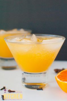 two glasses filled with orange juice on top of a white table next to an orange slice