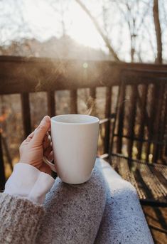 a person holding a coffee cup on top of a wooden bench with trees in the background