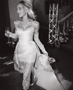 a woman in a white dress is holding a wine glass and walking down the street