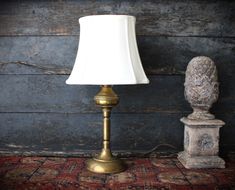 an antique brass table lamp with a white shade on it next to a carved stone urn